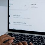 Hands typing on a laptop near New York location search screen.