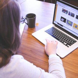 Person browsing the web on a MacBook at a wooden desk with a smartphone.